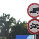Znaki drogowe zakazujące wjazdu ciężarówek i motocykli na tle drzew