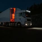 Biała ciężarówka nocą na górskiej drodze oświetlonej reflektorami
