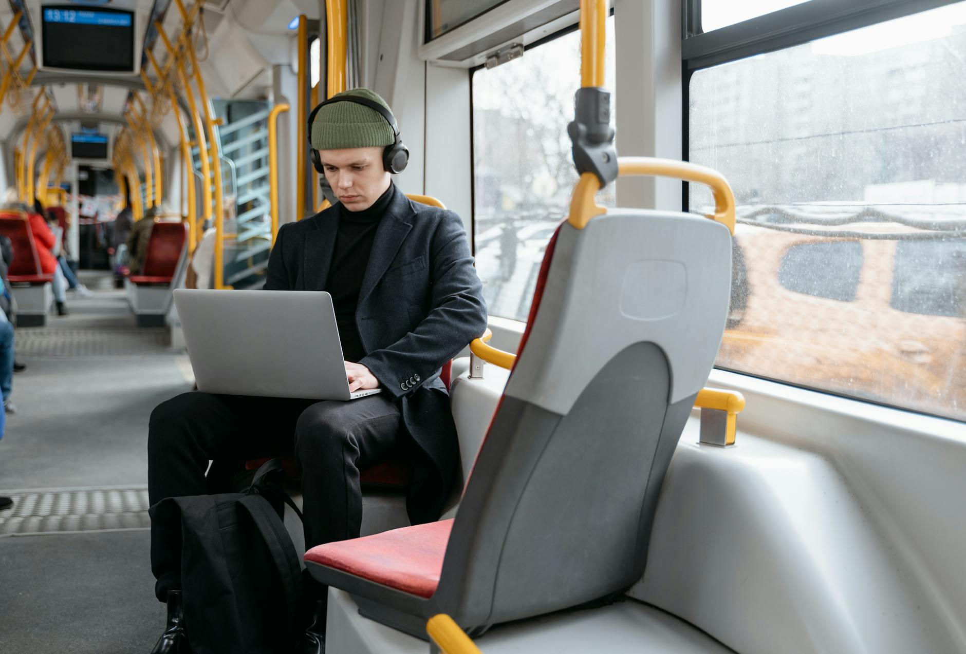 Mężczyzna w czarnym płaszczu pracuje na laptopie w tramwaju